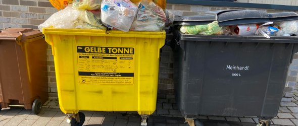 Drei volle Müllcontainer, die in einer Reihe stehen.