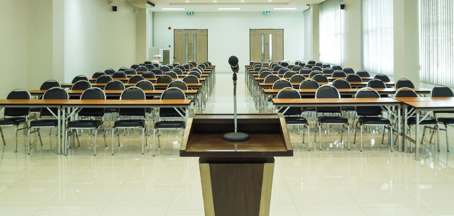 Ein Podest, in einem Sitzungssaal mit vielen Stühlen.