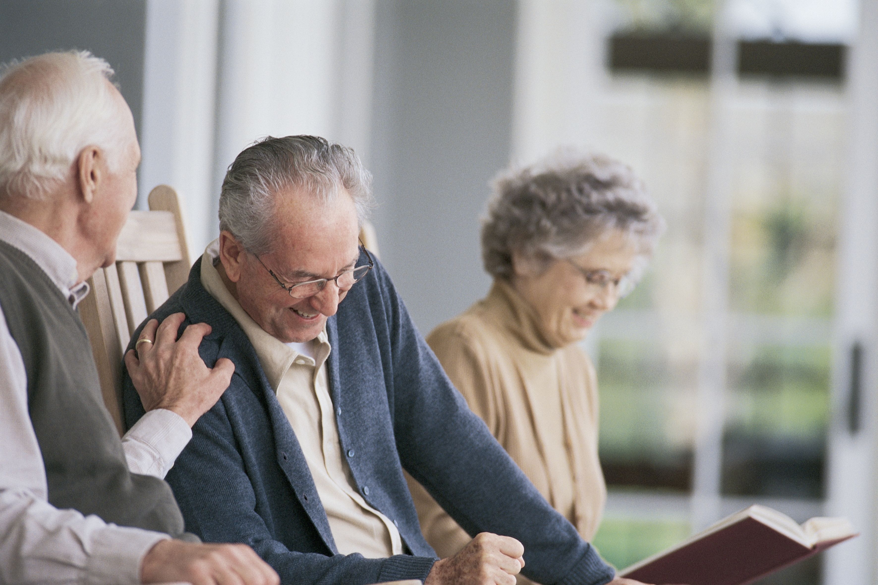 Drei Senioren, die sitzen und sich unterhalten. Im Hintergrund liest jemand.