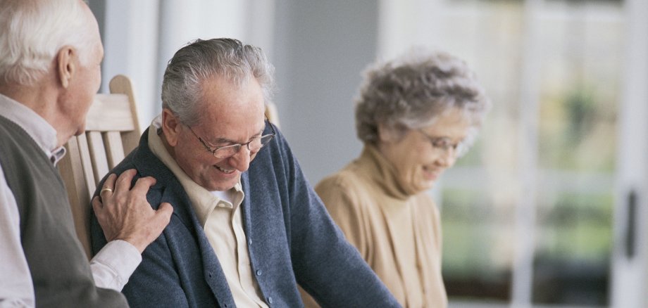 Drei Senioren, die sitzen und sich unterhalten. Im Hintergrund liest jemand.