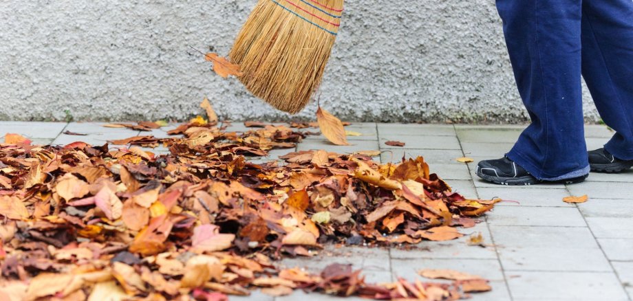 Nasses Laub wird vom Gehsteig gefegt