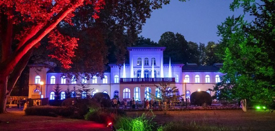 Badehaus beleuchtet in blau und weiß, Bäume rot und grün angeleuchtet