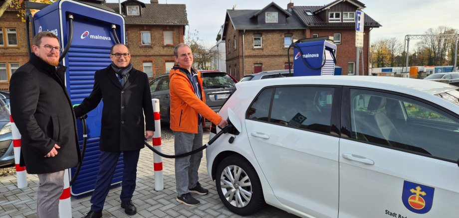 Mainova-Schnellladesäule Kevin Bornath, Mainova-Kommunalmanager, Bürgermeister Dr. Frank Blasch und Detlef Schümann, Klimaschutzbeauftragter der Stadt, (v.l.n.r.) bei einem Vororttermin an den neuen Schnellladesäulen.